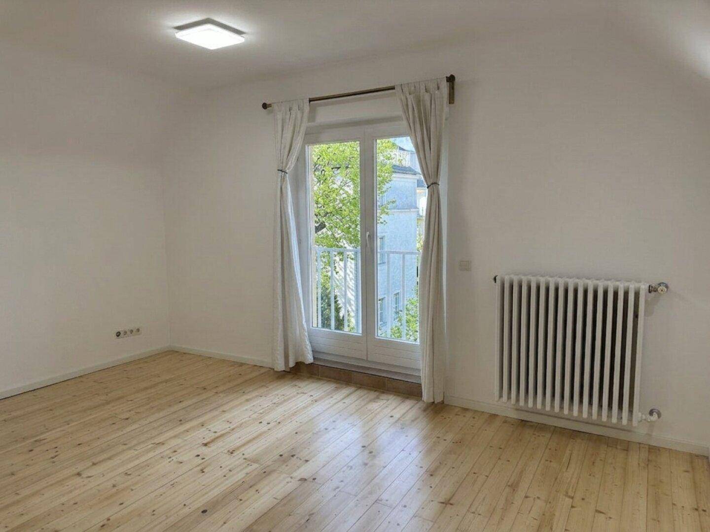 Heller Raum mit Holzboden und großem Fenster, das viel Tageslicht hereinlässt.