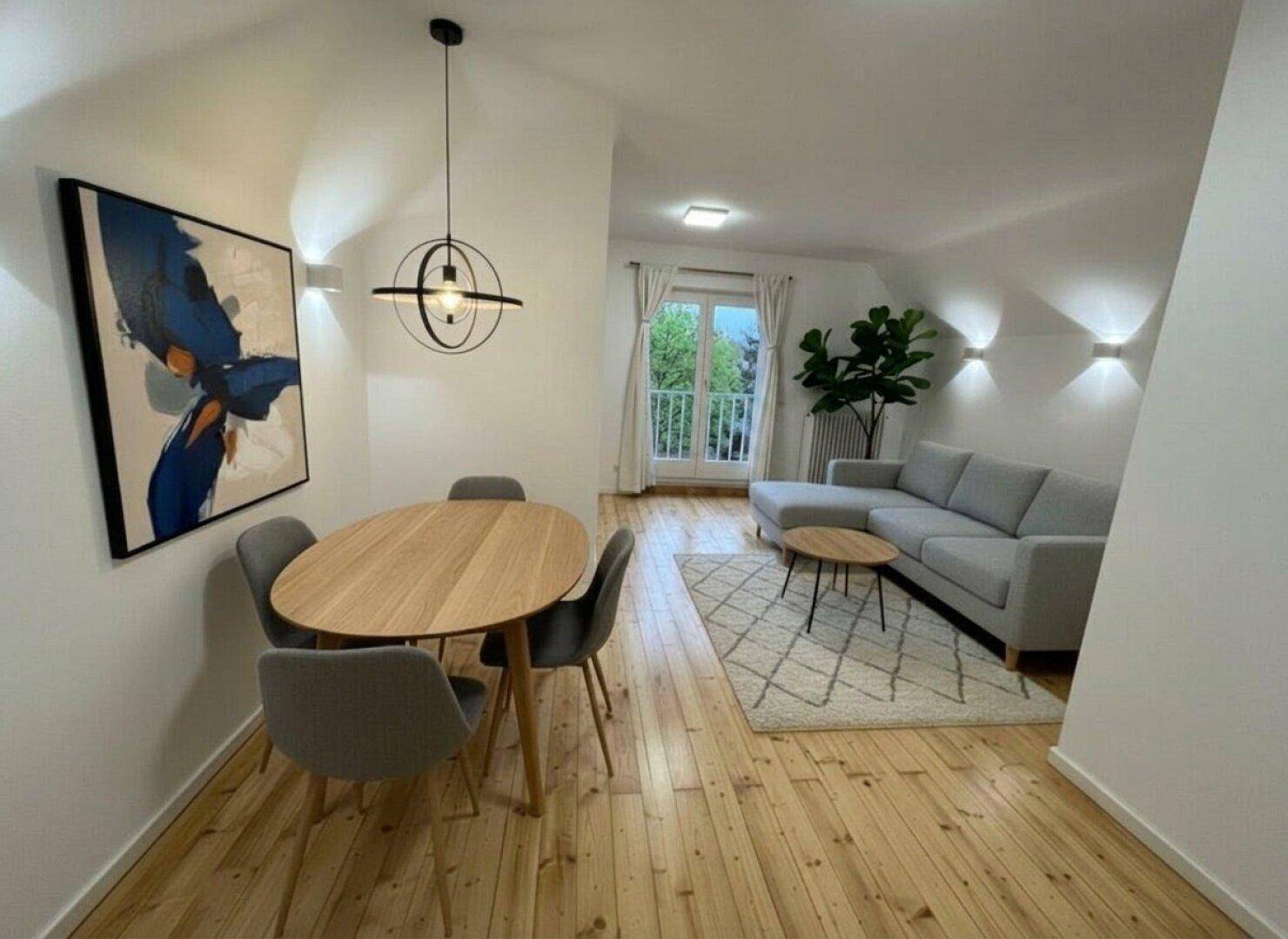 Heller Wohn- und Essbereich mit Holzboden, modernem Mobiliar und Zugang zum Balkon.