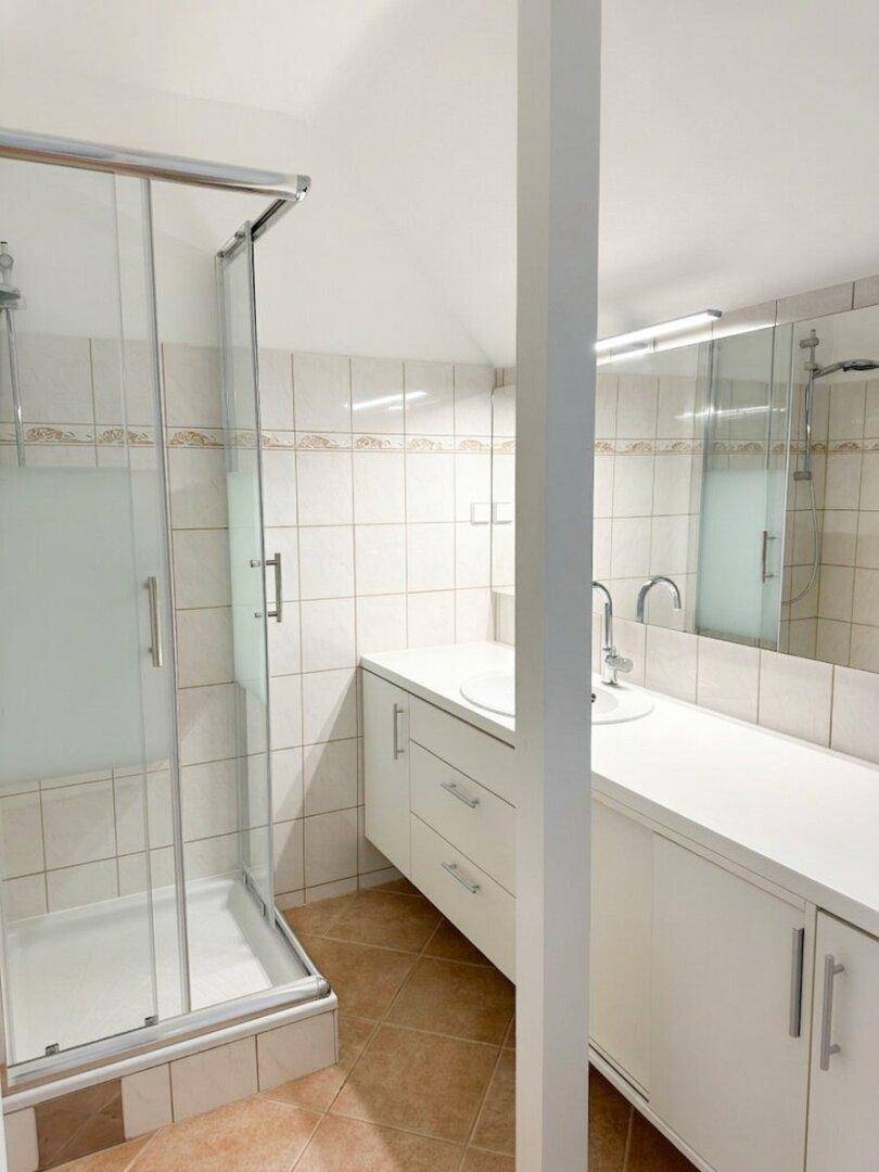 Badezimmer mit Duschkabine, Waschtisch und hellen Fliesen.