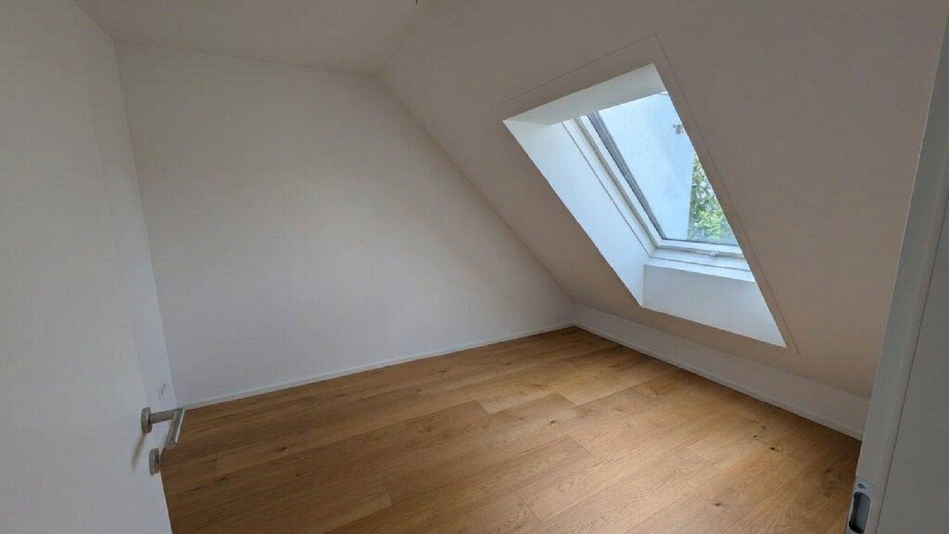 Gemütliches Schlafzimmer im Dachgeschoss mit Holzboden und einem großen Dachfenster für viel Licht.