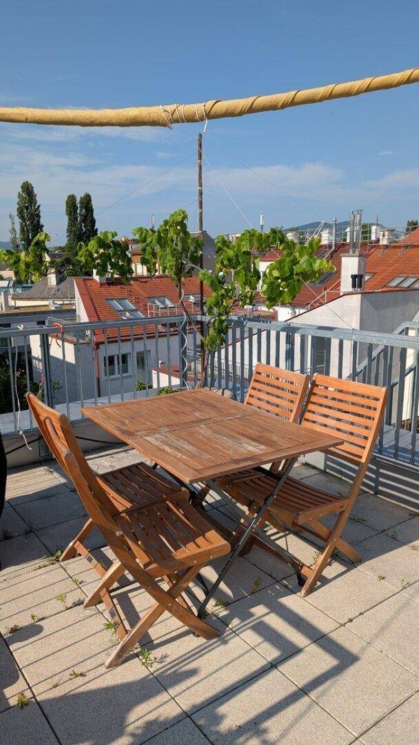 Sonnige Dachterrasse mit Holztisch und Stühlen, ideal für Mahlzeiten im Freien mit Weitblick.