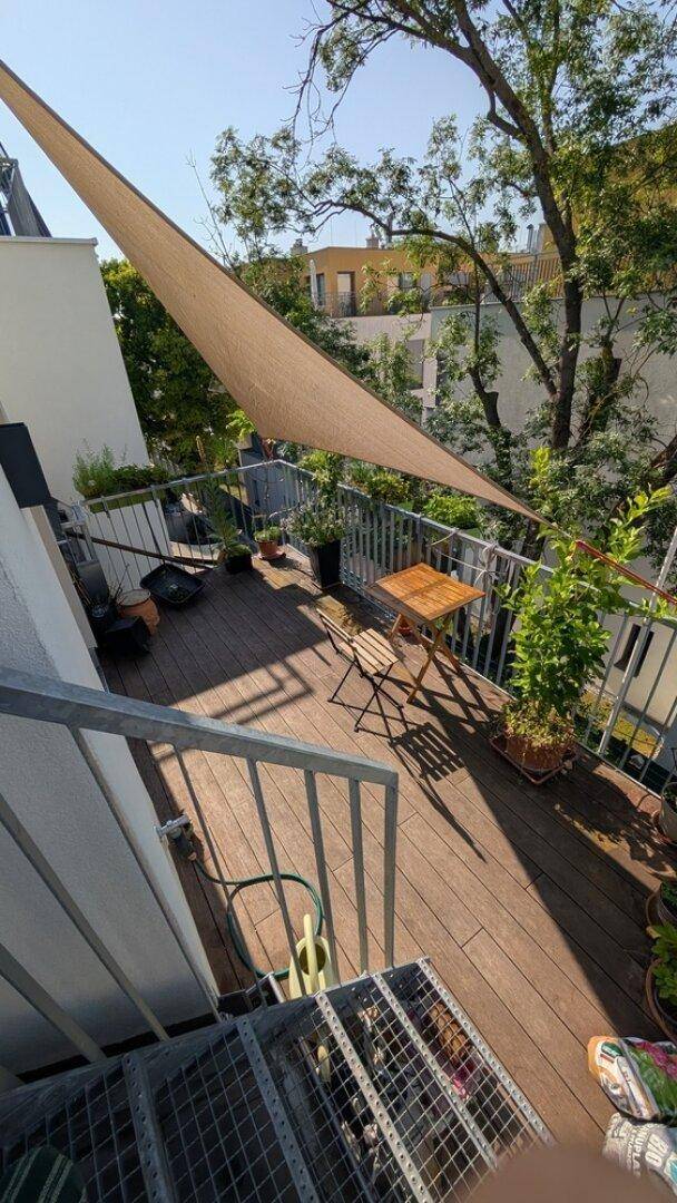 Helle Dachterrasse mit Holzbelag, Sonnensegel und Blick auf die umliegenden Gebäude und Bäume.