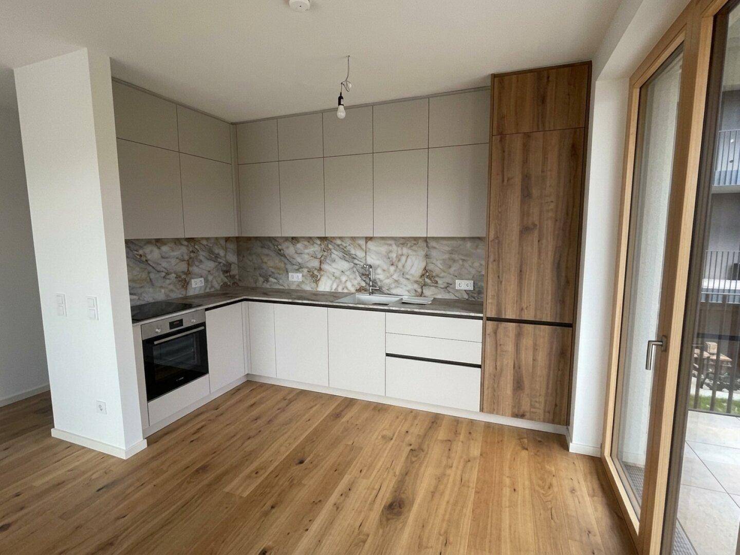 Moderne Einbauküche mit hellgrauen und holzfarbenen Schränken, Marmor-Rückwand und Holzboden.