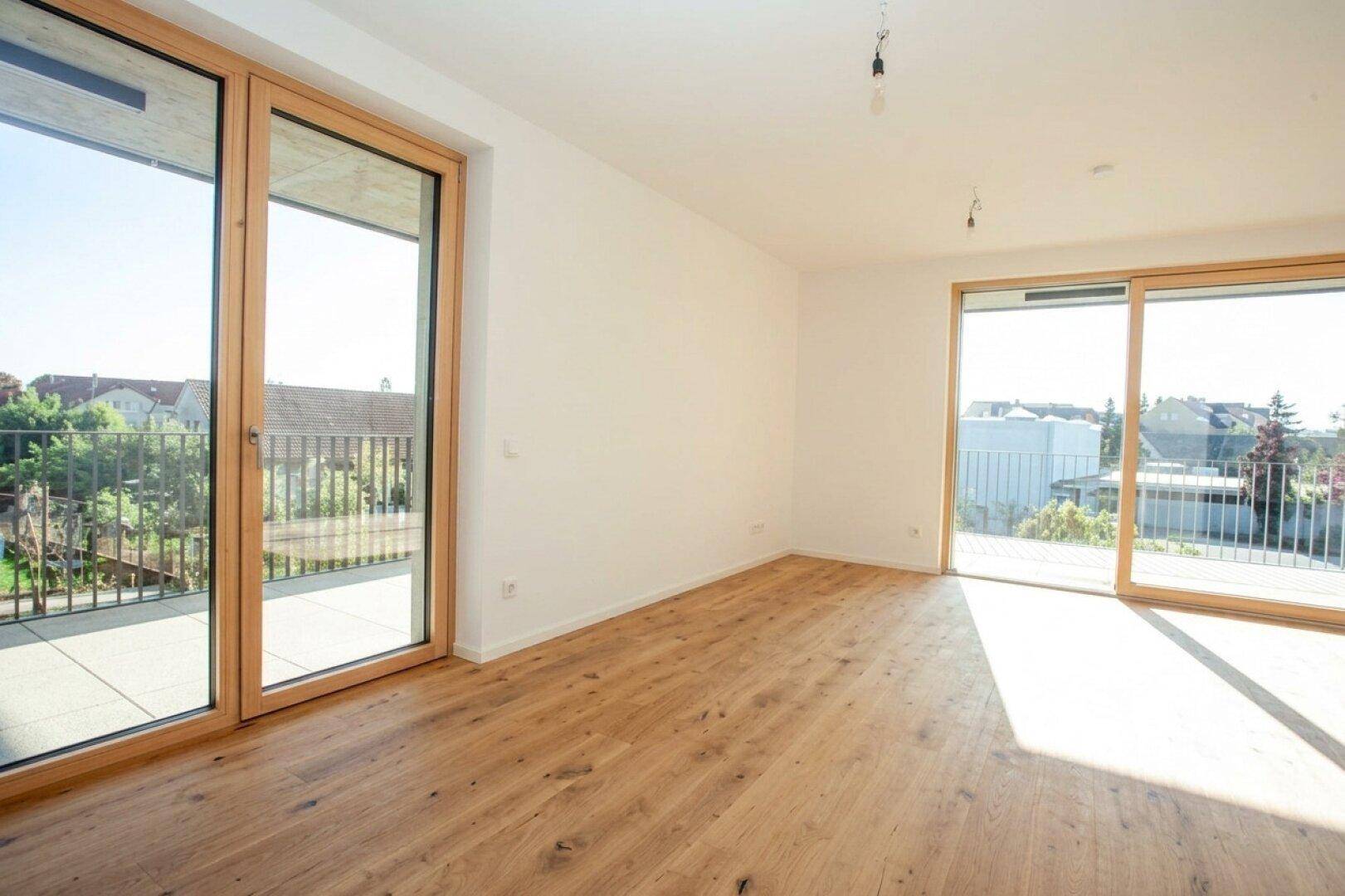 Lichtdurchfluteter Raum mit Holzboden und zwei großen Balkonzugängen, ideal für Wohn- oder Schlafzimmer.