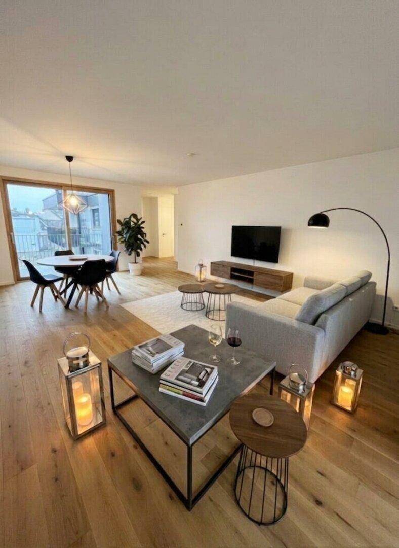 Modern eingerichteter Wohn-Essbereich mit Holzboden, bequemer Couch und Esstisch am Fenster.