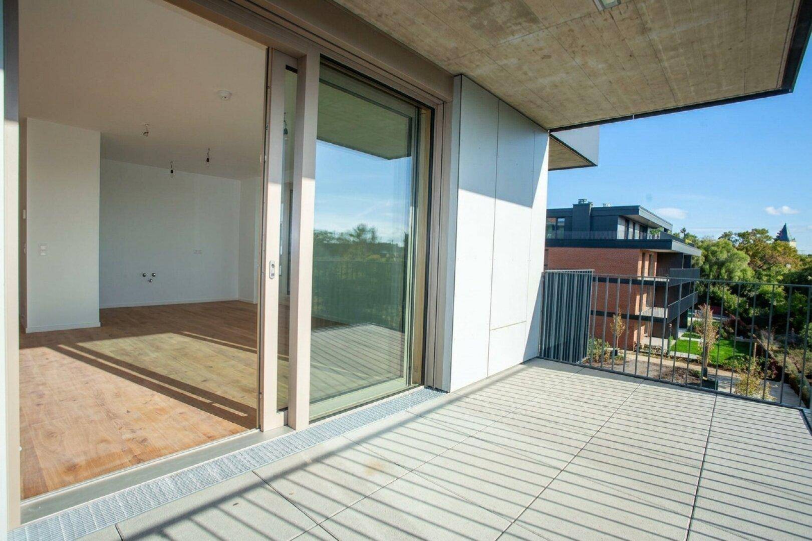 Moderner Balkon mit Fliesenboden und Blick auf die umliegenden Neubauten und Grünflächen.
