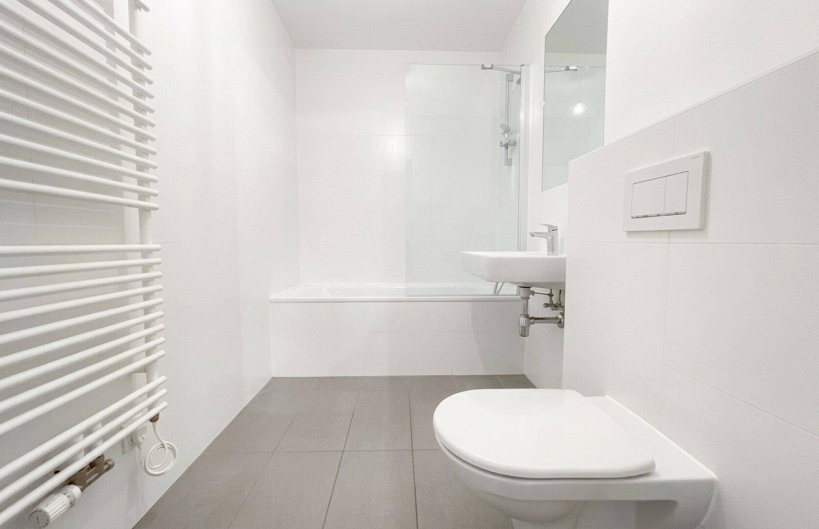 Modernes Badezimmer mit weißen Fliesen, Badewanne, WC, Waschbecken und beheiztem Handtuchhalter.