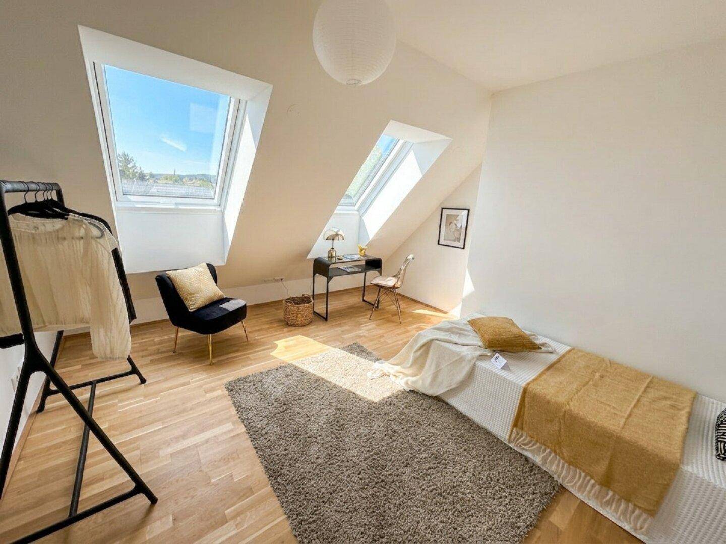 Helles Schlafzimmer mit Dachschrägen, Holzboden und zwei großen Dachfenstern für viel Tageslicht.