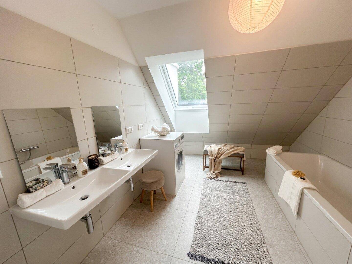 Modernes Badezimmer mit Doppelwaschbecken, Badewanne, Waschmaschine und Dachfenster unter der Schräge.