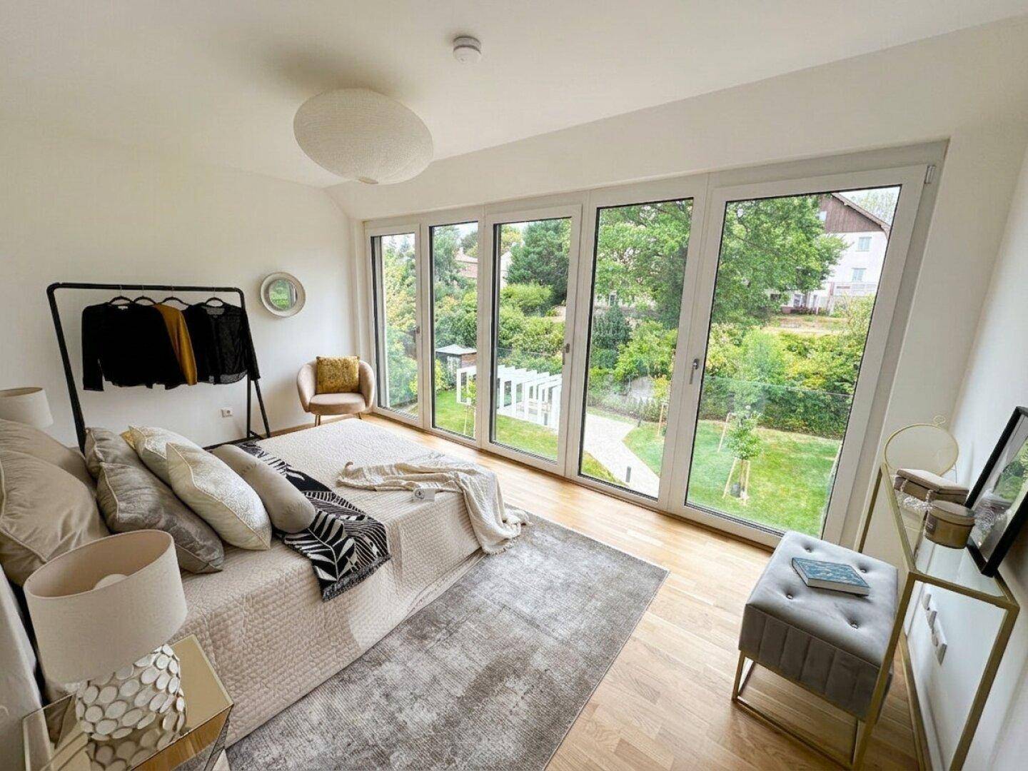 Helles Schlafzimmer mit großen Fenstern, die einen direkten Blick in den grünen Garten bieten.