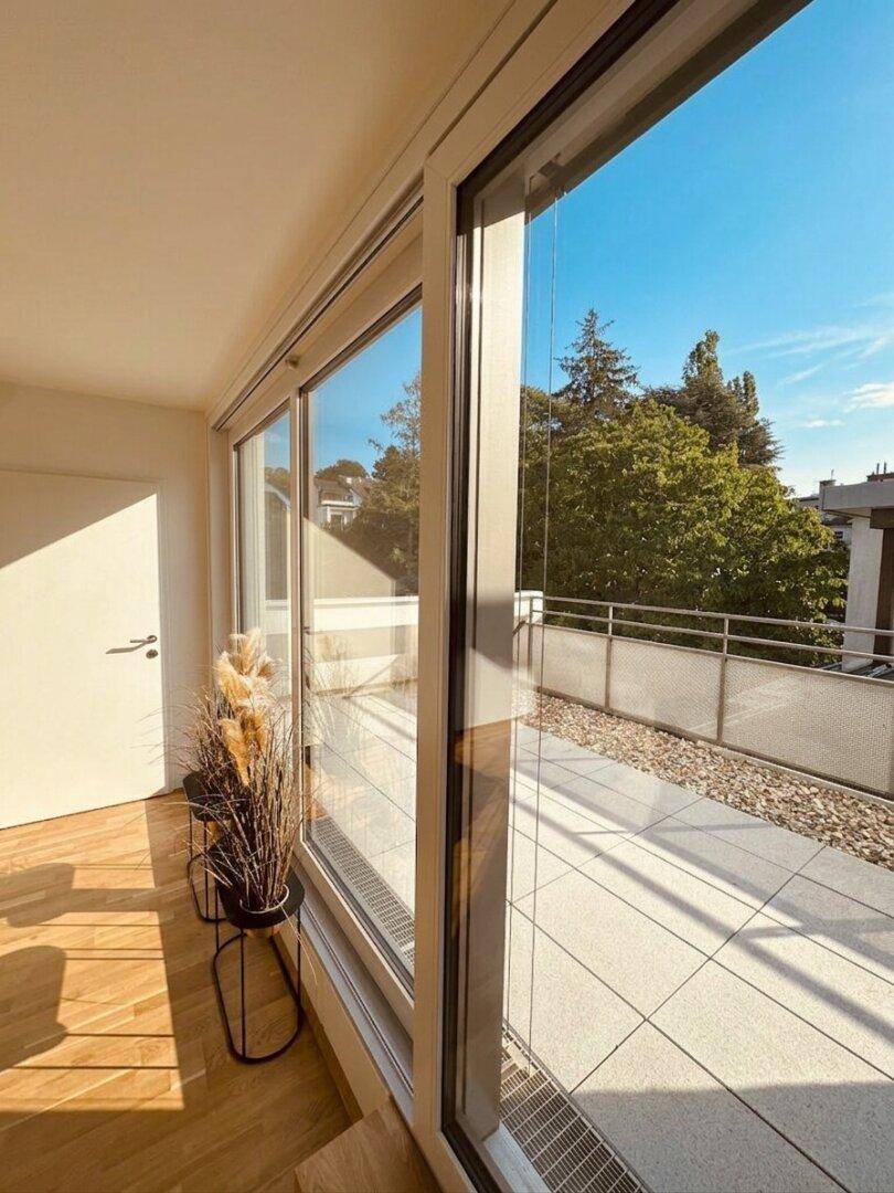 Große, sonnige Terrasse mit Fliesenboden und weitem Blick ins Grüne, zugänglich durch Glasschiebetüren.