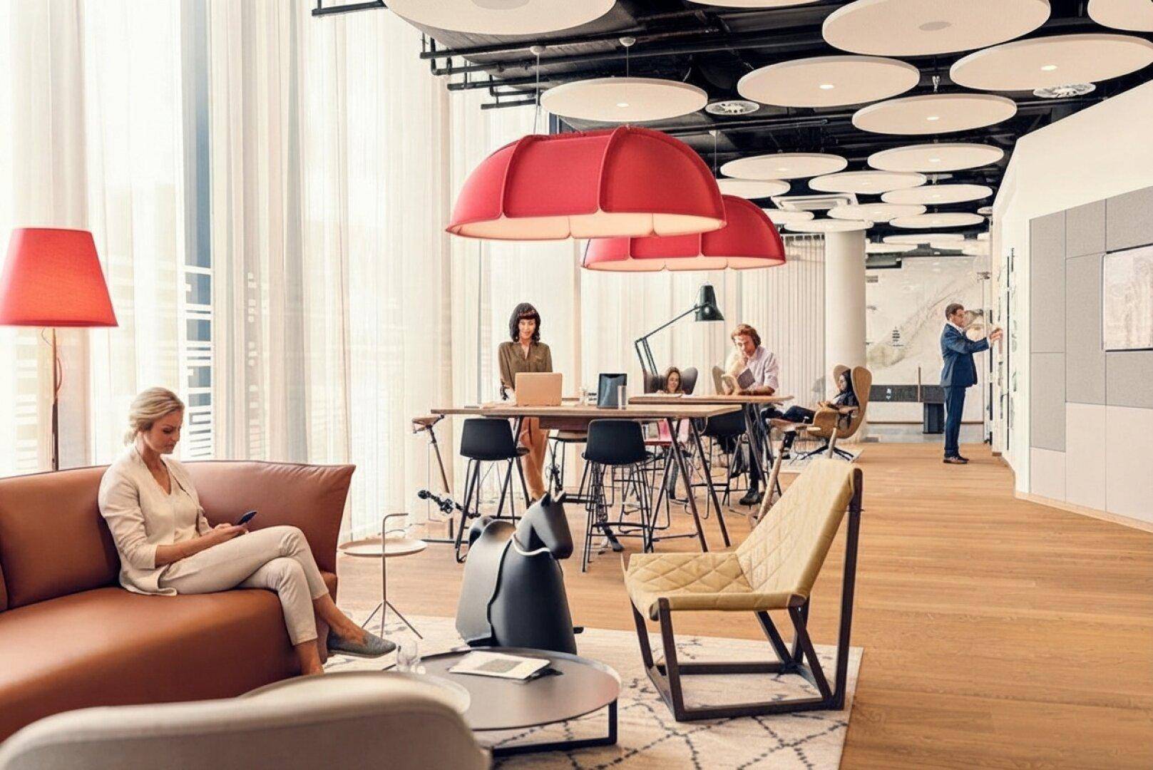 Stilvolle Lounge-Zone in einem modernen Bürogebäude mit bequemen Sofas, hohen Tischen und dekorativen Leuchten.