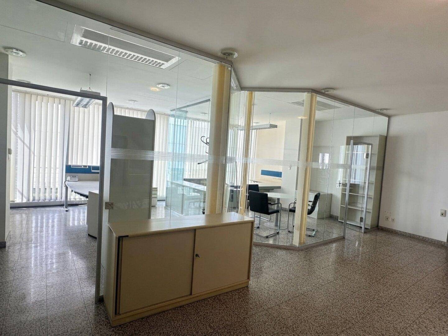 Geräumiges Büro mit modernen Glaswänden, funktionalen Möbeln und Terrazzoboden.