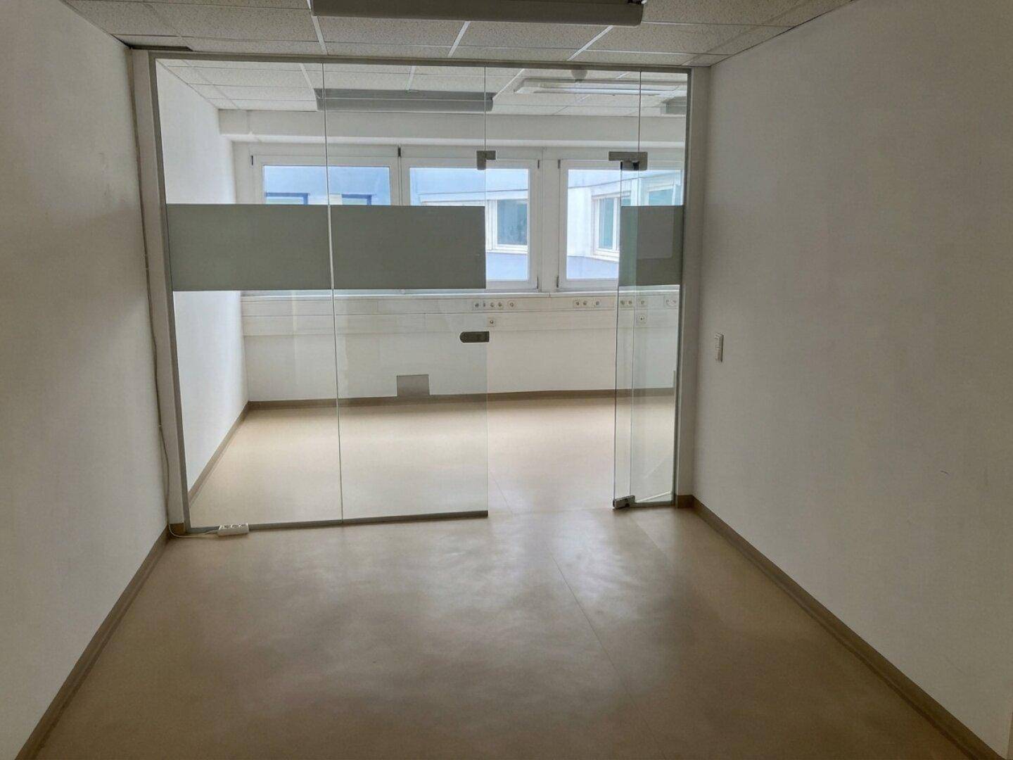 Leerer Büroraum mit Glaswänden und einem hellen Bodenbelag, bereit zur Einrichtung.