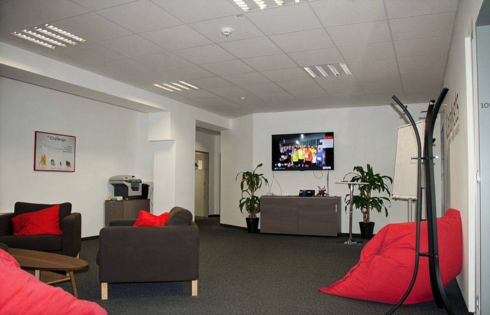 Gemütlicher Aufenthaltsraum mit Fernseher, bequemen Sitzgelegenheiten und Pflanzen.