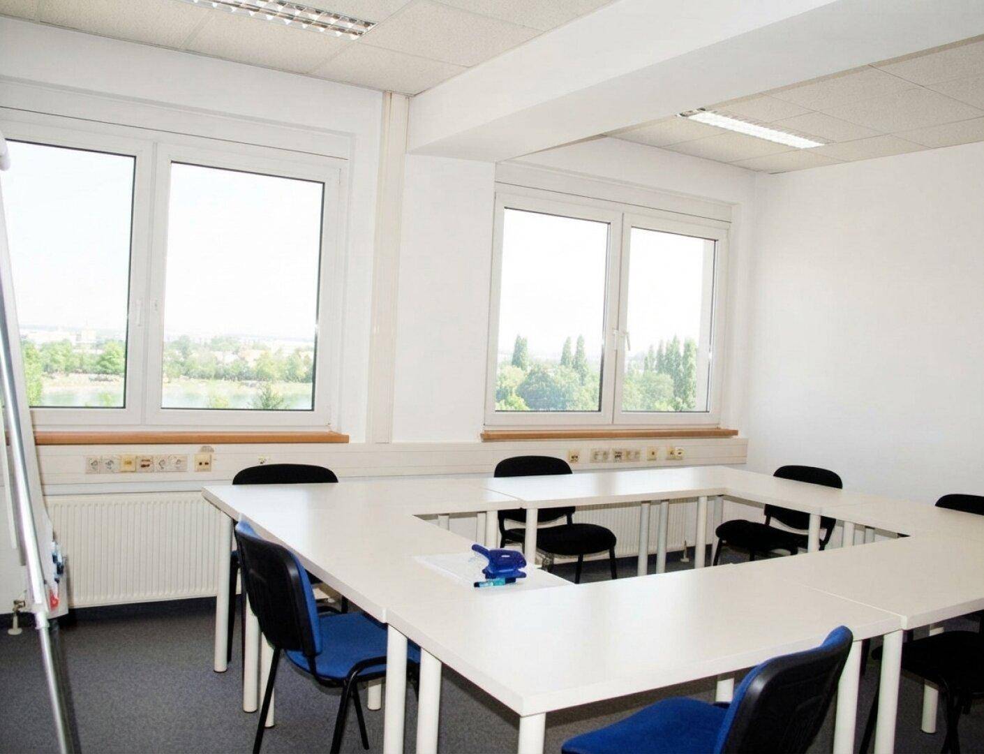 Konferenzraum mit U-förmigem Tisch, blauen Stühlen und großen Fenstern mit Ausblick.