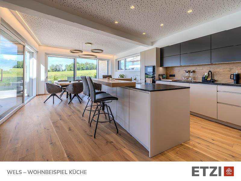 Moderne Küche mit Kochinsel, Holzboden und Essbereich mit Blick ins Grüne.