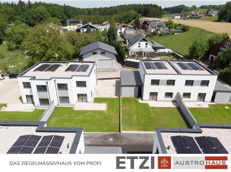 Luftaufnahme von Doppelhäusern mit Photovoltaikanlagen und angrenzenden Gärten.