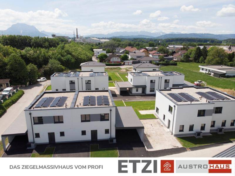 Luftaufnahme einer modernen Wohnsiedlung mit Photovoltaikanlagen auf den Dächern und Bergblick.