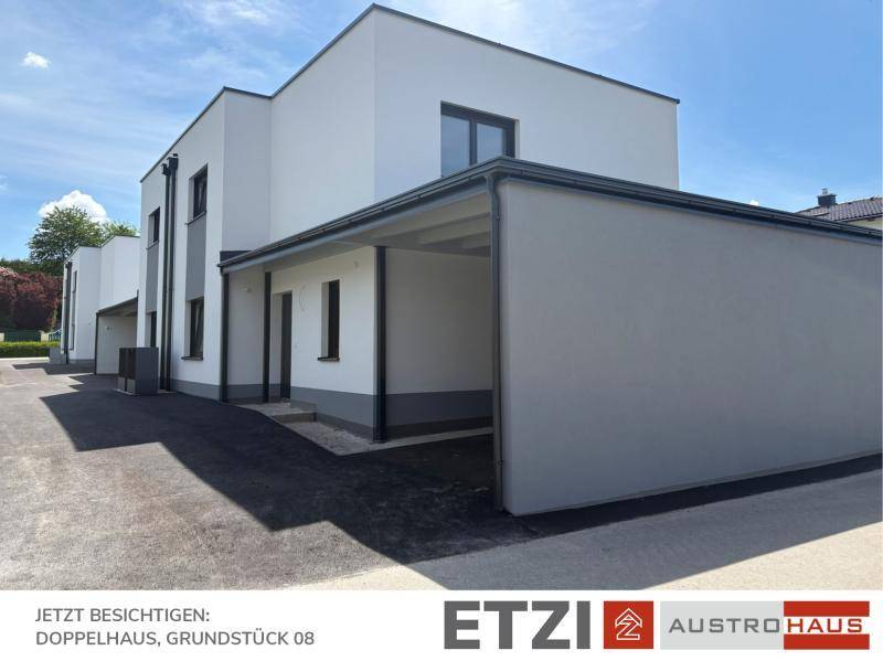 Modernes Doppelhaus mit Carport und weißer Fassade, umgeben von einer gepflegten Außenanlage.