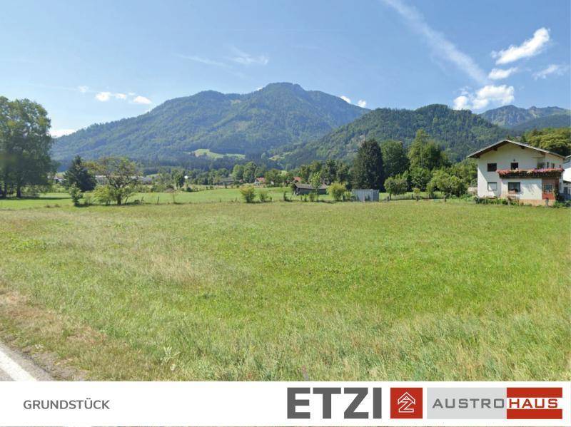 Weitläufige Grünflächen mit einem Haus am Rande und beeindruckendem Alpenpanorama im Hintergrund.