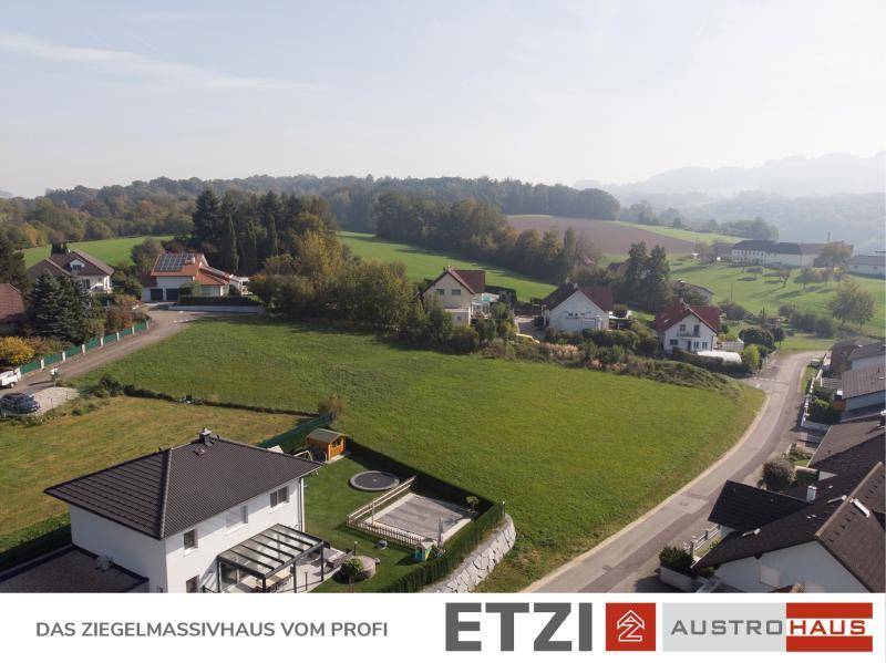 Luftaufnahme einer weitläufigen Grünfläche, umgeben von Wohnhäusern und einer hügeligen Landschaft.
