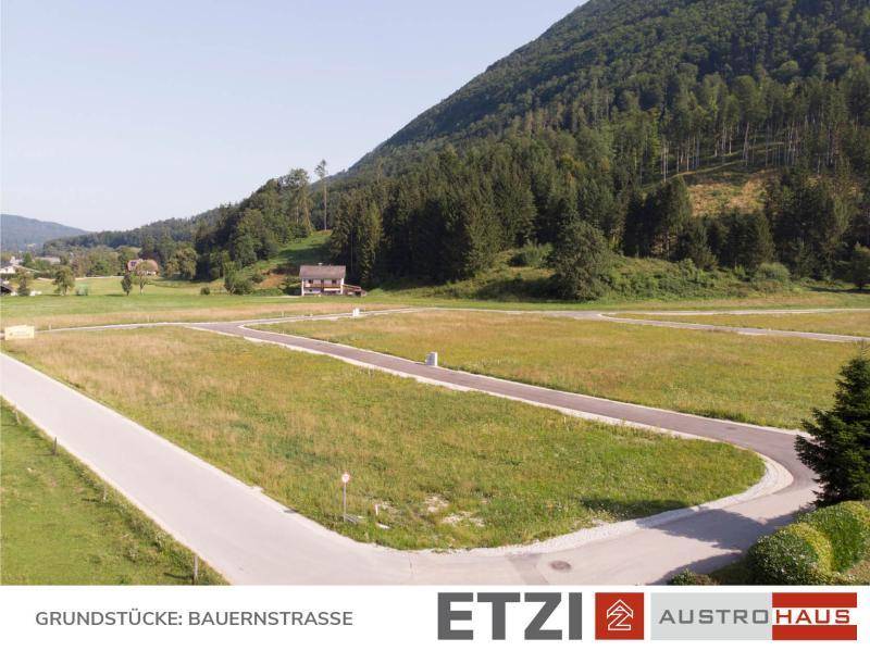 Weitläufige Ansicht des Baugebietes mit grünen Parzellen und umliegender Berglandschaft.
