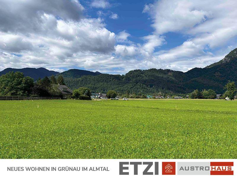 Panoramablick über grüne Wiesen und bewaldete Berge, mit Siedlung im Hintergrund.