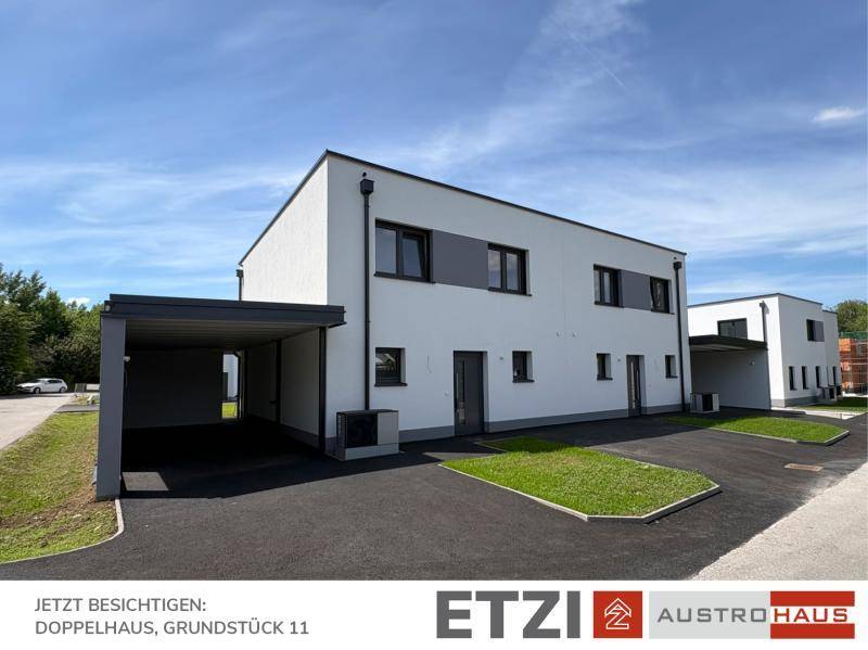 Modernes Doppelhaus mit Carport und gepflasterter Zufahrt unter blauem Himmel.