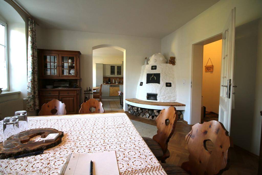 Rustikaler Essbereich mit Kachelofen und Holztisch, angrenzend an eine moderne Küche.