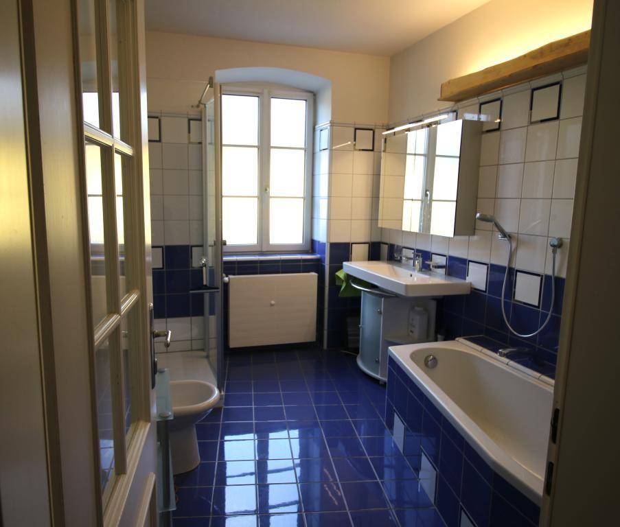 Helles Badezimmer mit blauen Fliesen, Badewanne, Dusche und Fenster, in gutem Zustand.