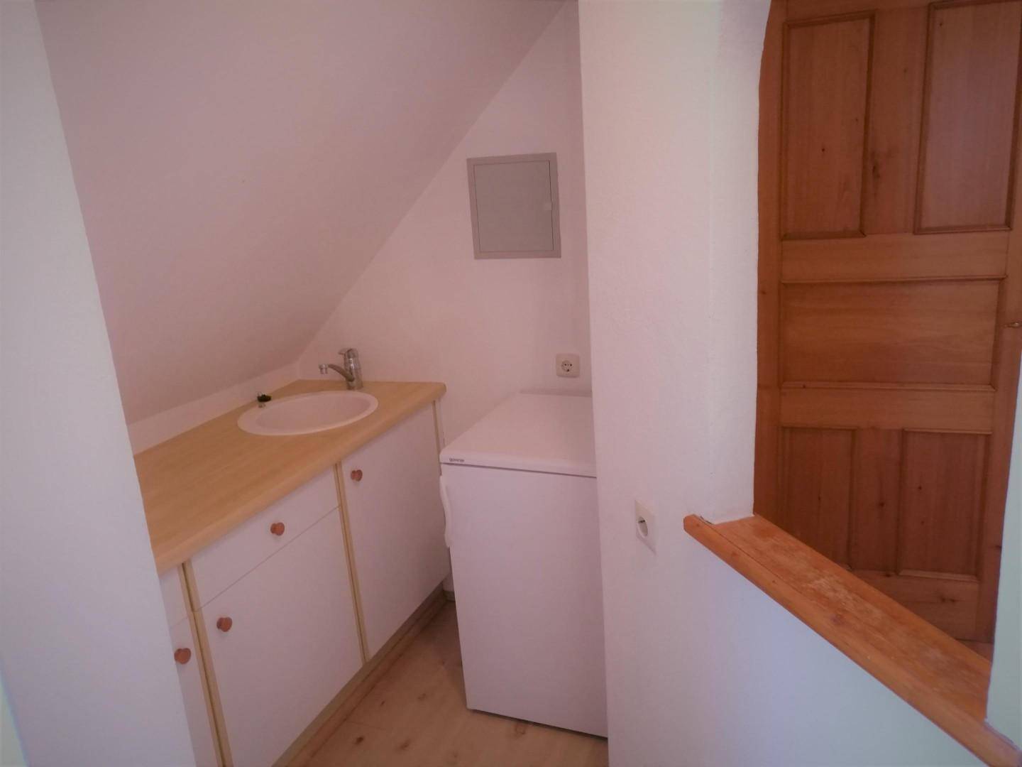 Kleiner Hauswirtschaftsraum mit Waschbecken, Unterschränken und Waschmaschine unter Dachschräge.
