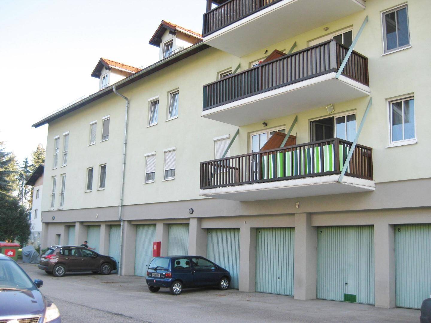 Gebäudeansicht mit Garagen im Erdgeschoss und darüberliegenden Balkonen mit Holzgeländer.