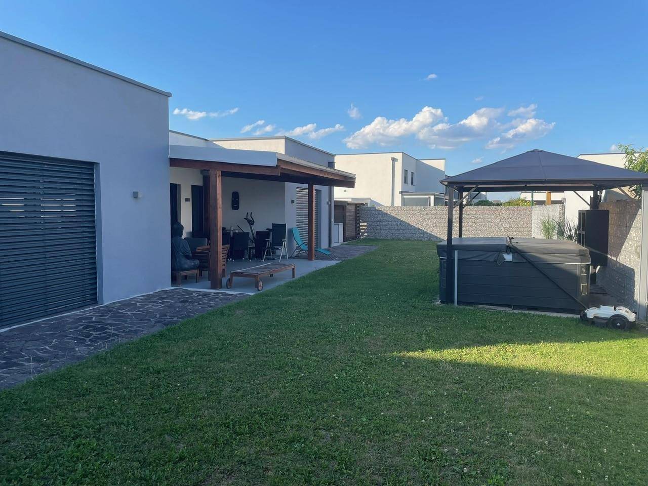 Gepflegter Gartenbereich mit überdachter Terrasse, Rasenfläche und Whirlpool unter einem Pavillon.