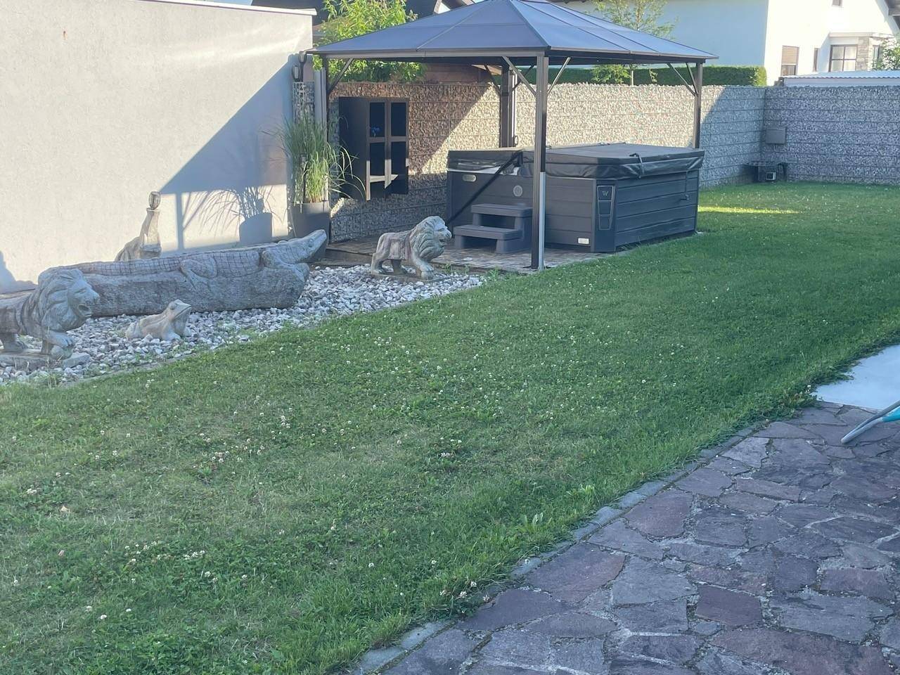 Detailansicht des Whirlpools unter einem Pavillon im Garten, umgeben von Rasen und Dekorationselementen.