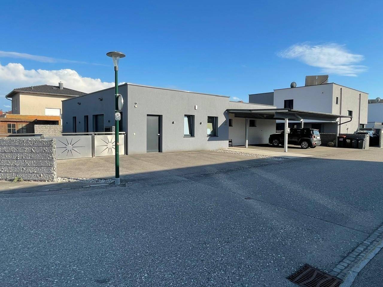 Vorderansicht des modernen Einfamilienhauses mit Eingangsbereich, Fenstern und Carport unter blauem Himmel.