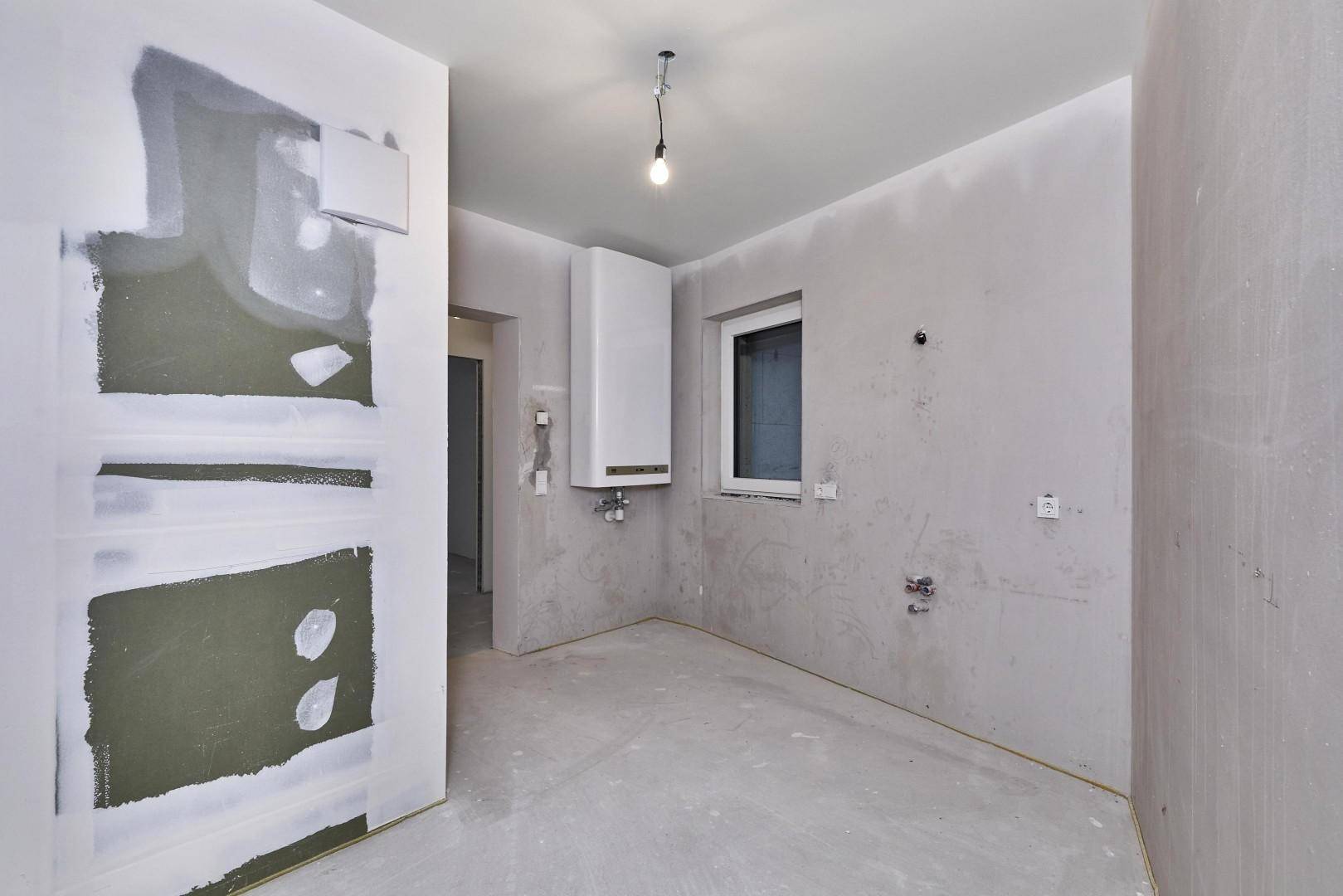 Unfertiger Hauswirtschaftsraum mit Heiztherme und Fenster, bereit für den Ausbau.