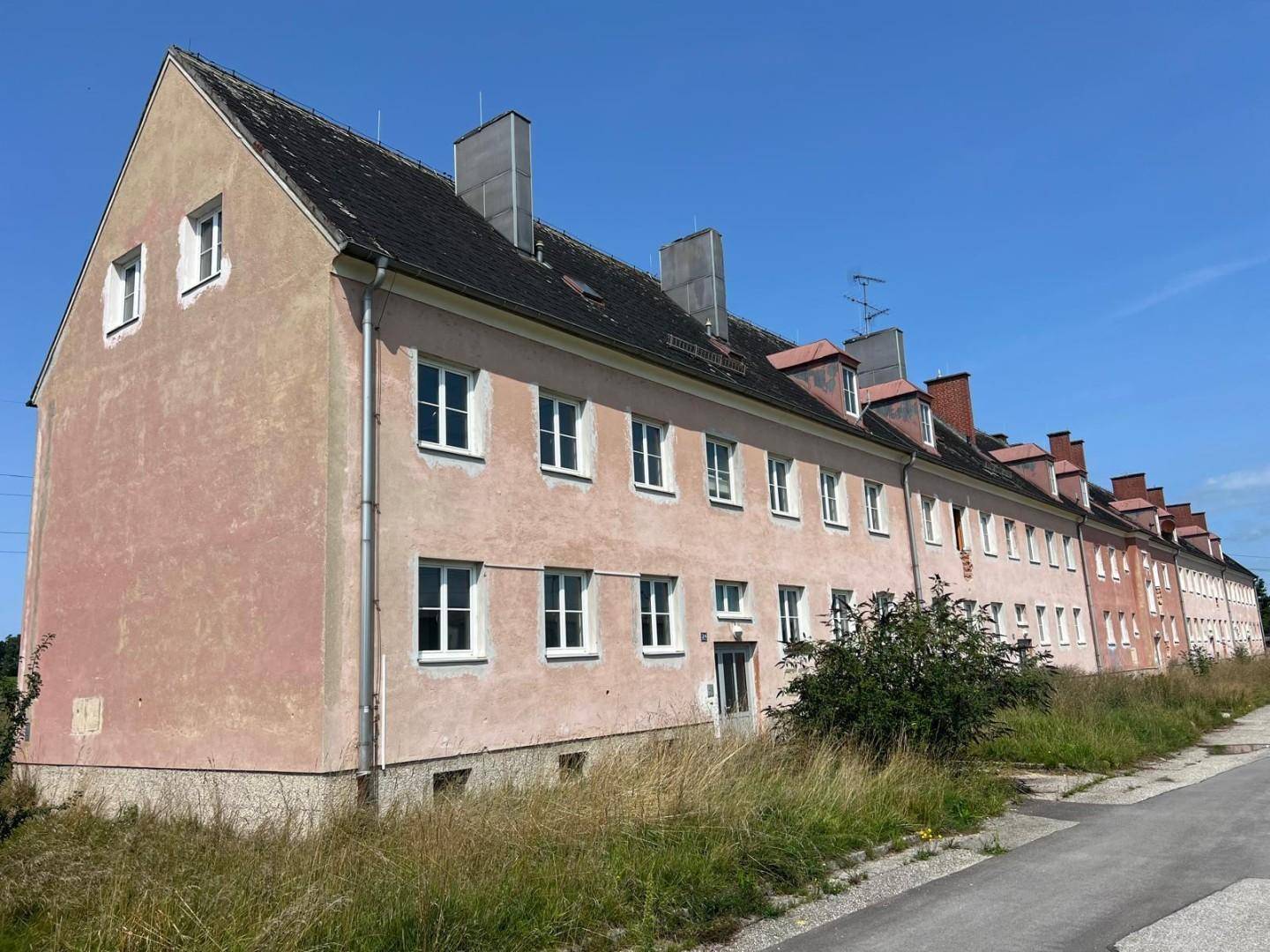 Seitenansicht eines langen Wohngebäudes mit verblasster Fassade und vielen Fenstern unter klarem Himmel.
