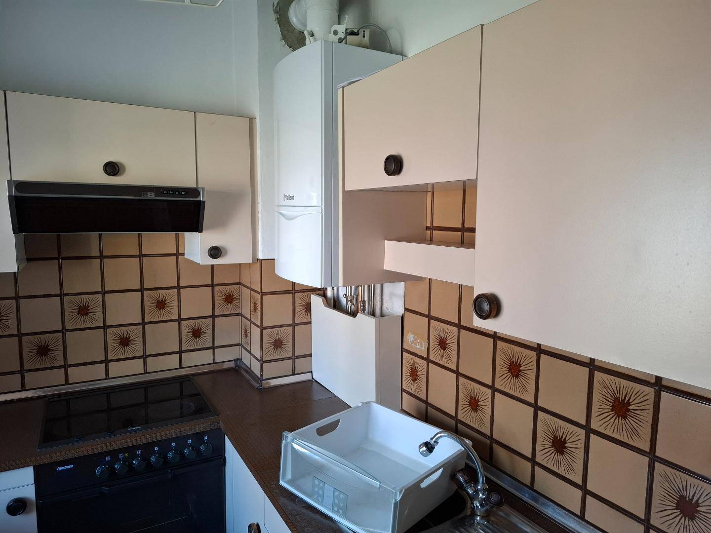 Küchenbereich mit Gastherme, Spüle und gemusterten Wandfliesen.