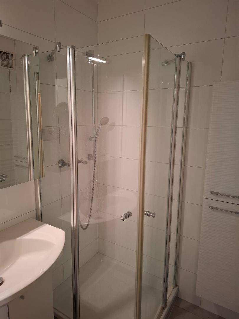 Badezimmer mit weiß gefliesten Wänden, Duschkabine und einem Waschbecken.