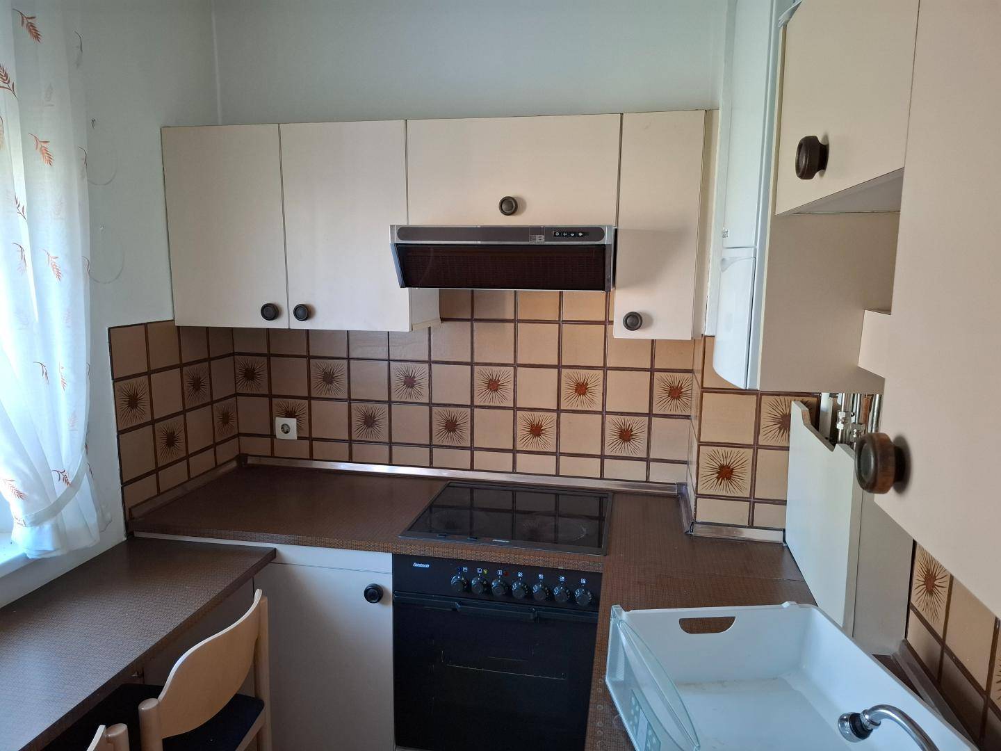 Küche mit beigen Schränken, gemusterten Fliesen und einem Elektroherd.