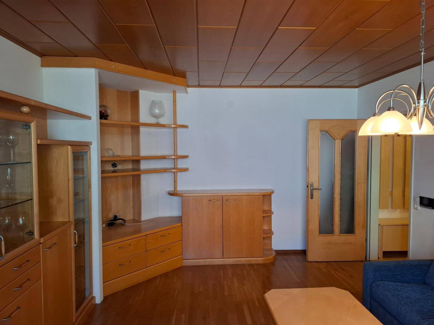 Helles Wohnzimmer mit Holzmöbeln, Parkettboden und einer passenden Holzdecke.