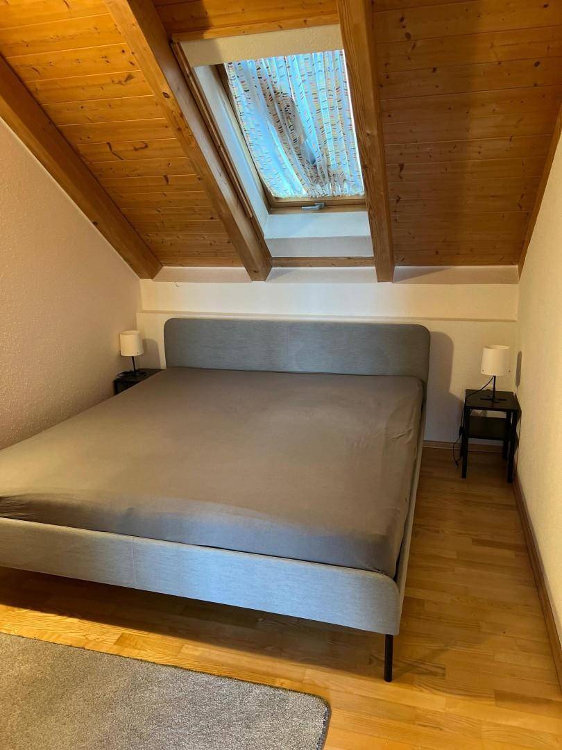Schlafzimmer im Dachgeschoss mit Holzbalken, Holzboden und einem Dachfenster für natürliches Licht.