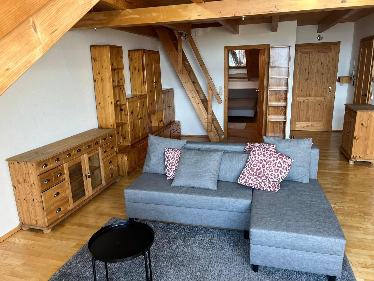 Gemütliches Wohnzimmer im Dachgeschoss mit Holzbalken, Sofa und Holzmöbeln.