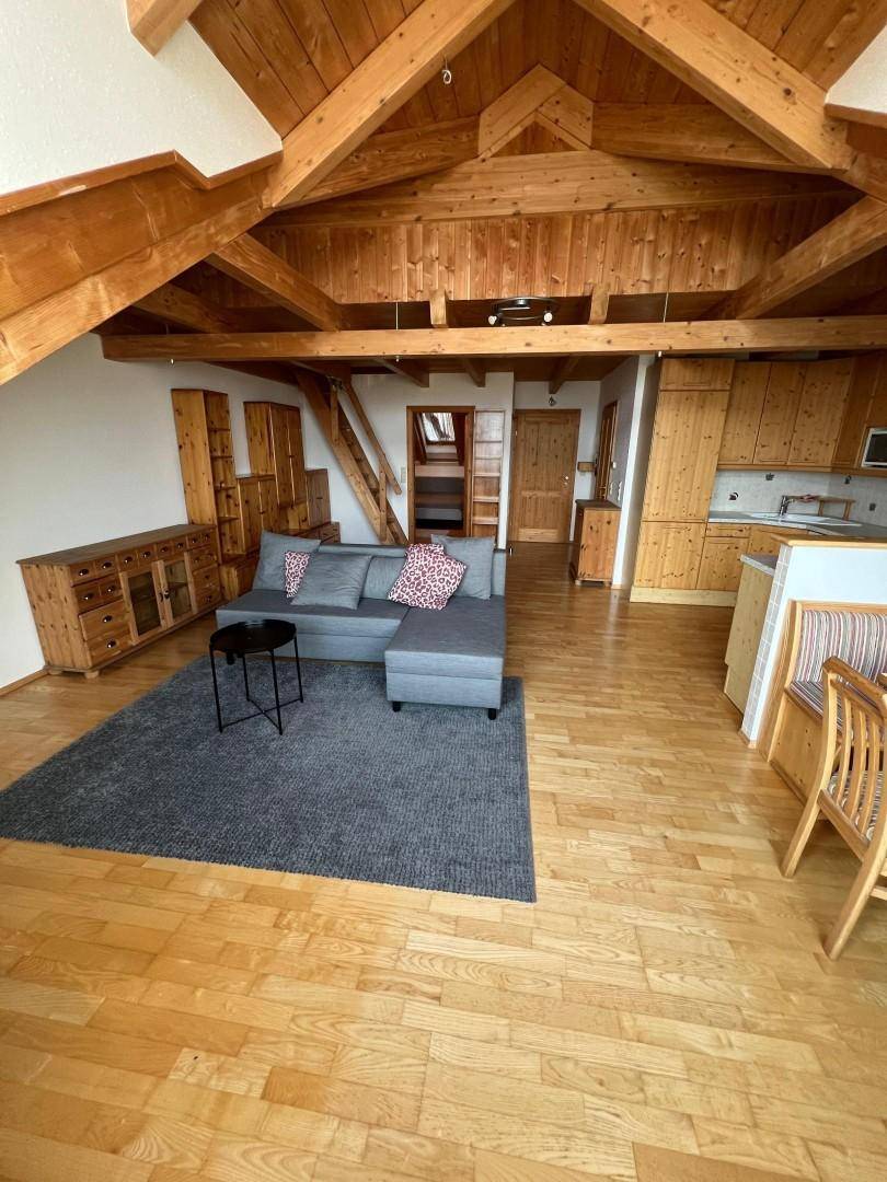 Offener Wohnbereich im Dachgeschoss mit Holzbalken, Sofa und Blick zur Küche.