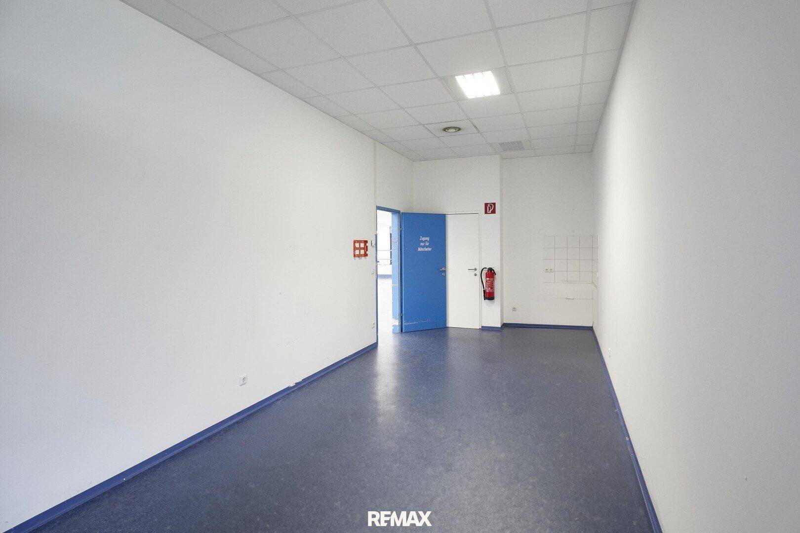 Kleinerer Raum innerhalb der Gewerbeeinheit mit weißen Wänden, blauem Boden und einer blauen Tür, möglicherweise ein Büro.