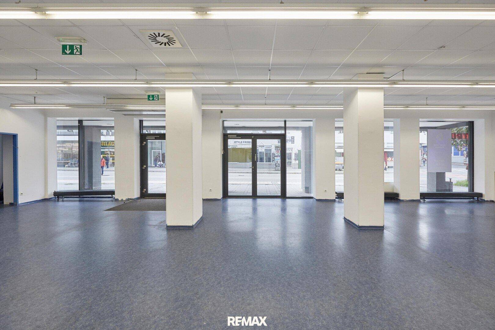 Weitläufiger Gewerberaum mit offener Gestaltung, Säulen und großen Fensterfronten zur Straße, bietet viel Tageslicht.