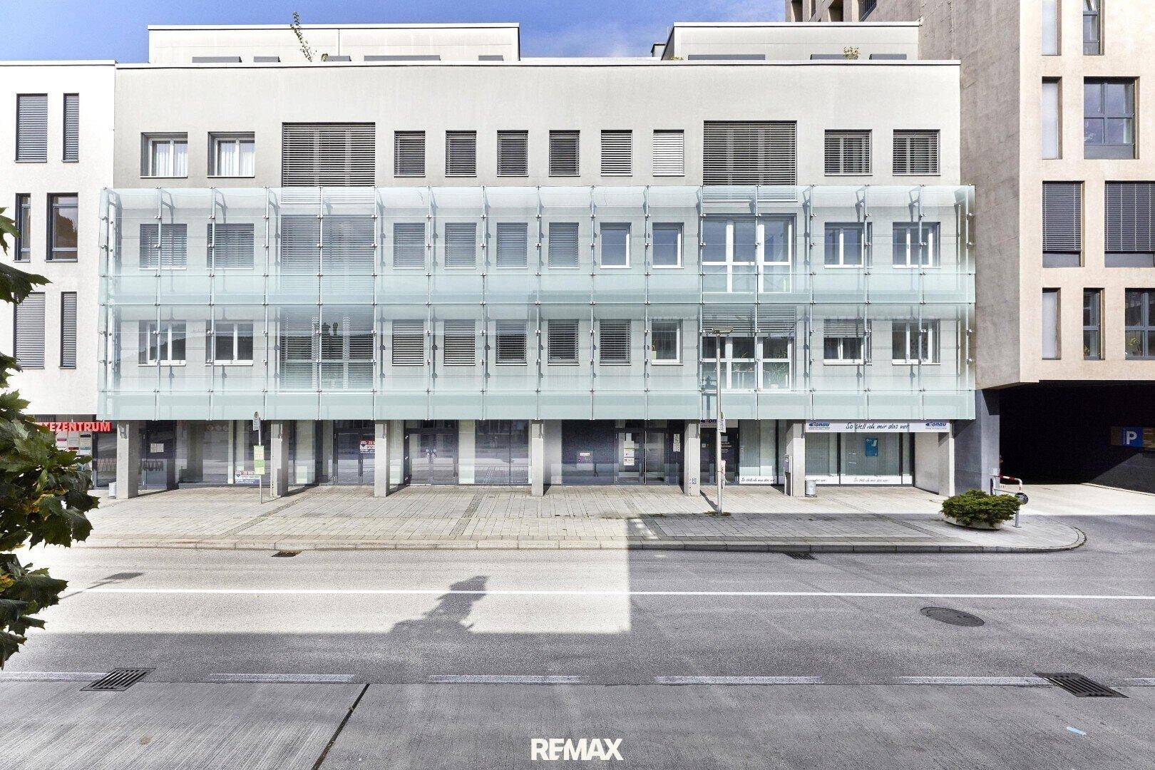 Gesamtansicht der modernen Geschäftsfassade mit mehreren Etagen und markanten Glasstrukturen, von der Straße aus gesehen.