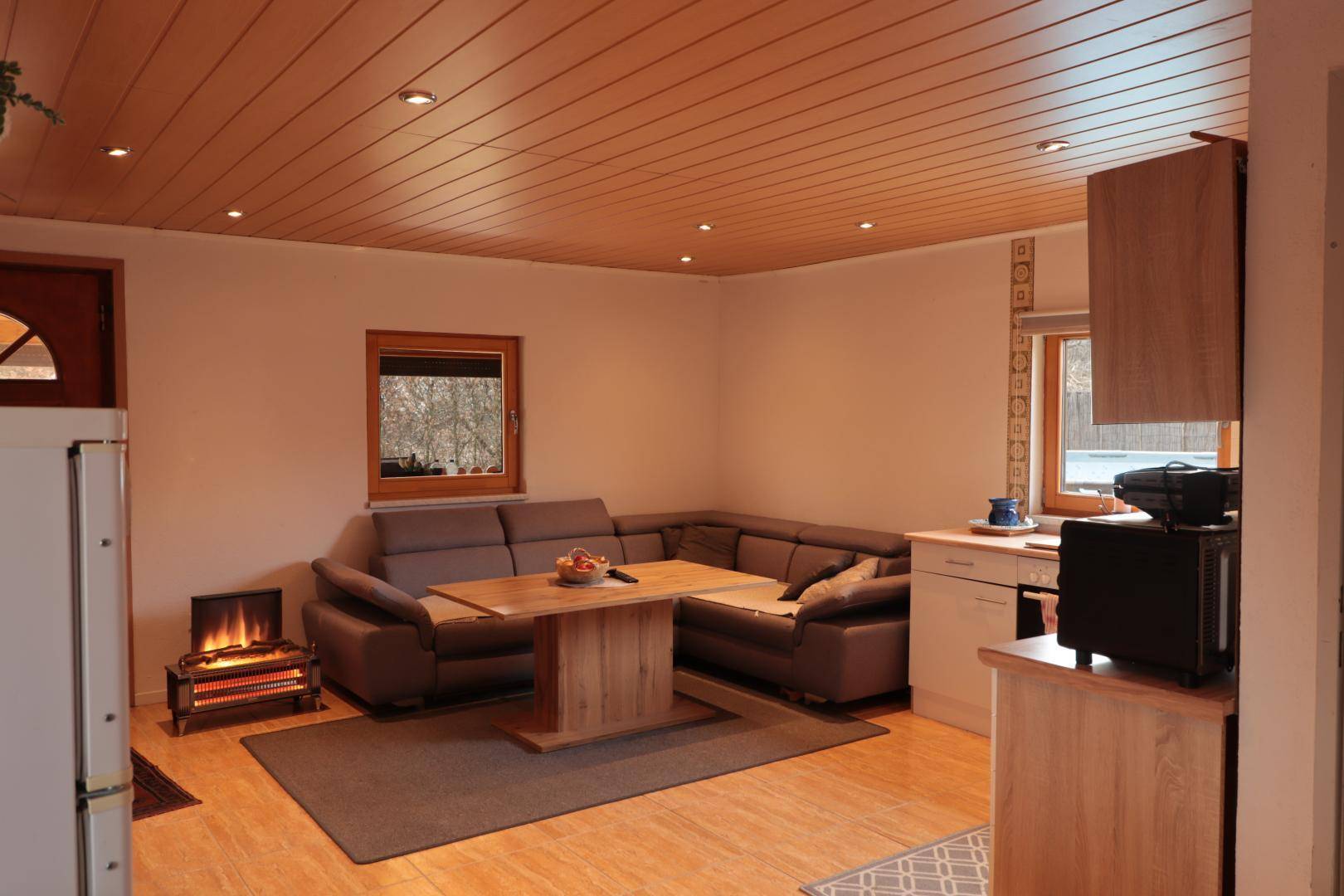 Gemütlicher Wohn- und Essbereich mit Holztäfelung an der Decke und kleiner Küchenzeile.