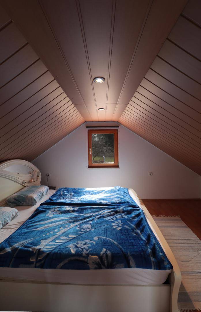 Schlafzimmer im Dachgeschoss mit Holztäfelung, Dachschräge und kleinem Fenster.